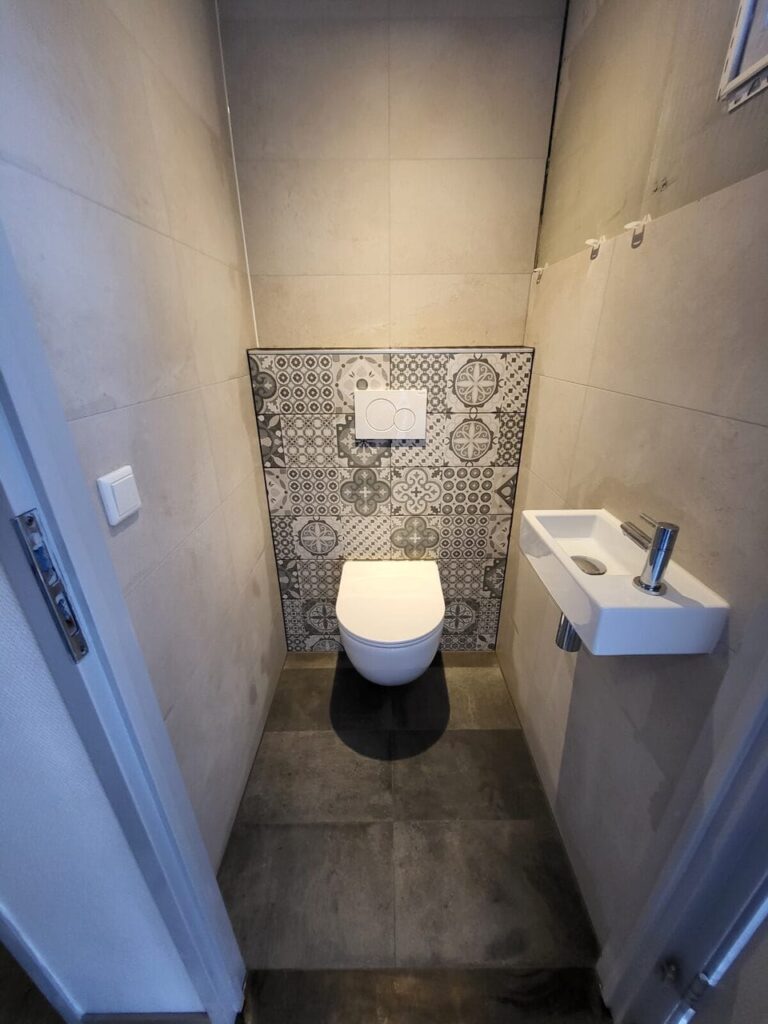 Separate toilet with grey walls, patterned accent tiles and a wall-hung toilet with corner basin