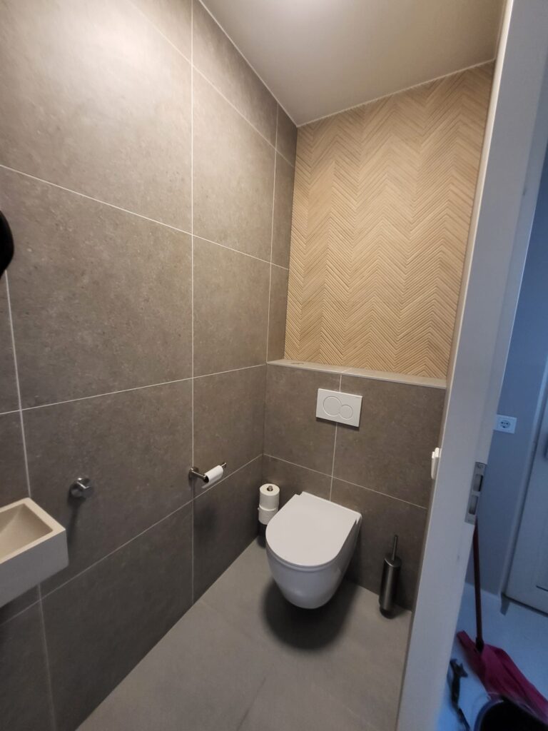 Separate toilet with grey tiles, herringbone wood-effect accent wall and wall-hung toilet
