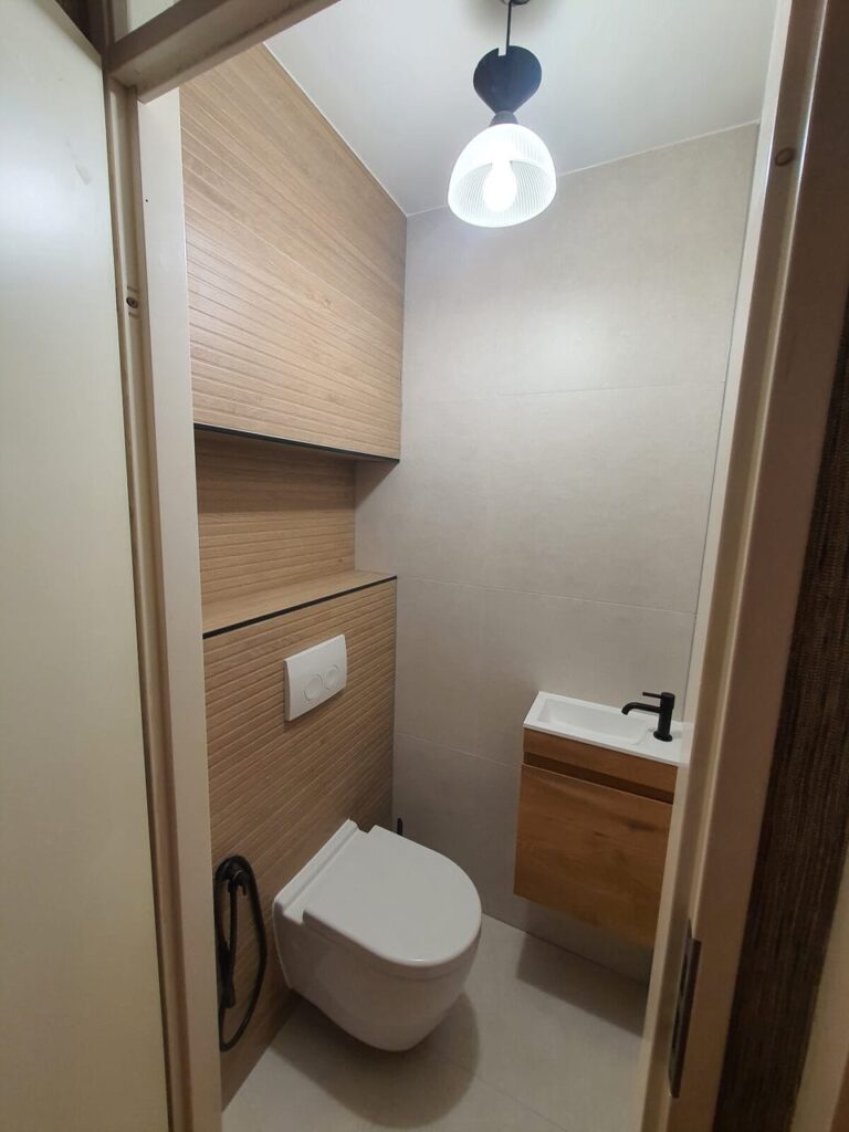 Renovated toilet with wood-effect wall panel, wall-hung toilet and small vanity with black basin