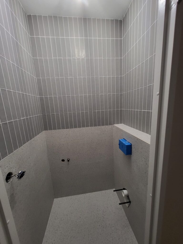 Shower enclosure during renovation with grey wall tiles being installed