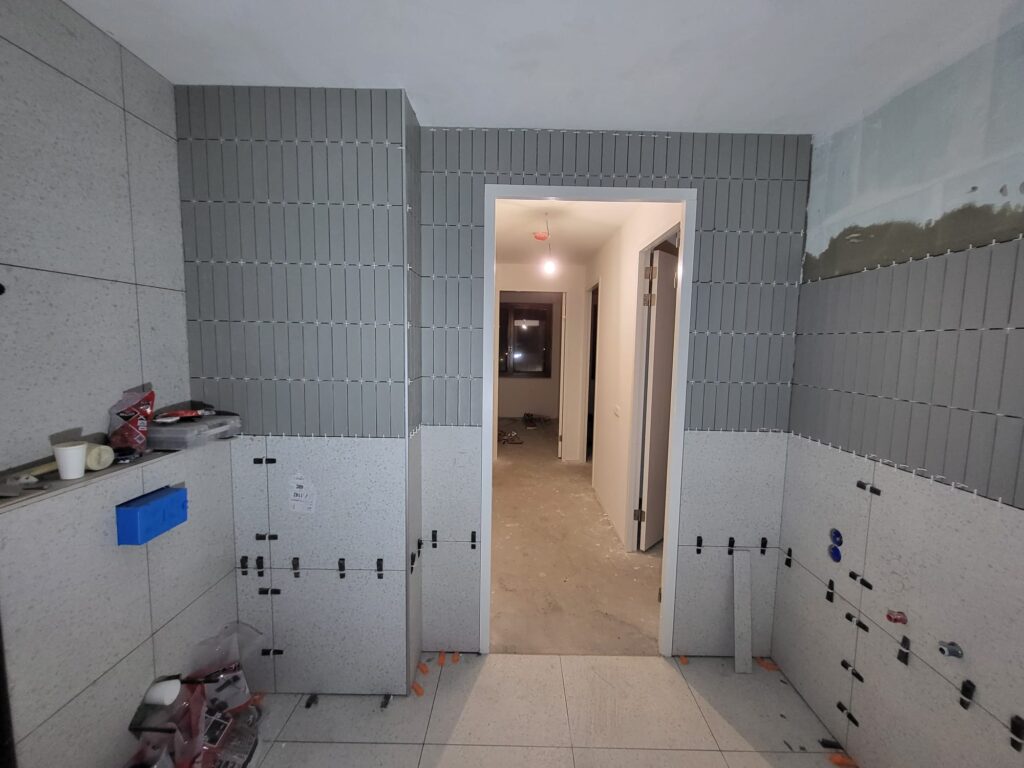 Bathroom during renovation with grey wall tiles being fitted and plumbing in progress