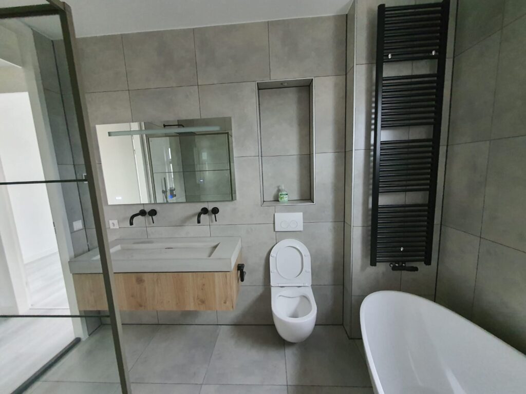 Renovated bathroom with grey tiles, floating wooden vanity, large mirror, black towel radiator, freestanding bath and walk-in shower