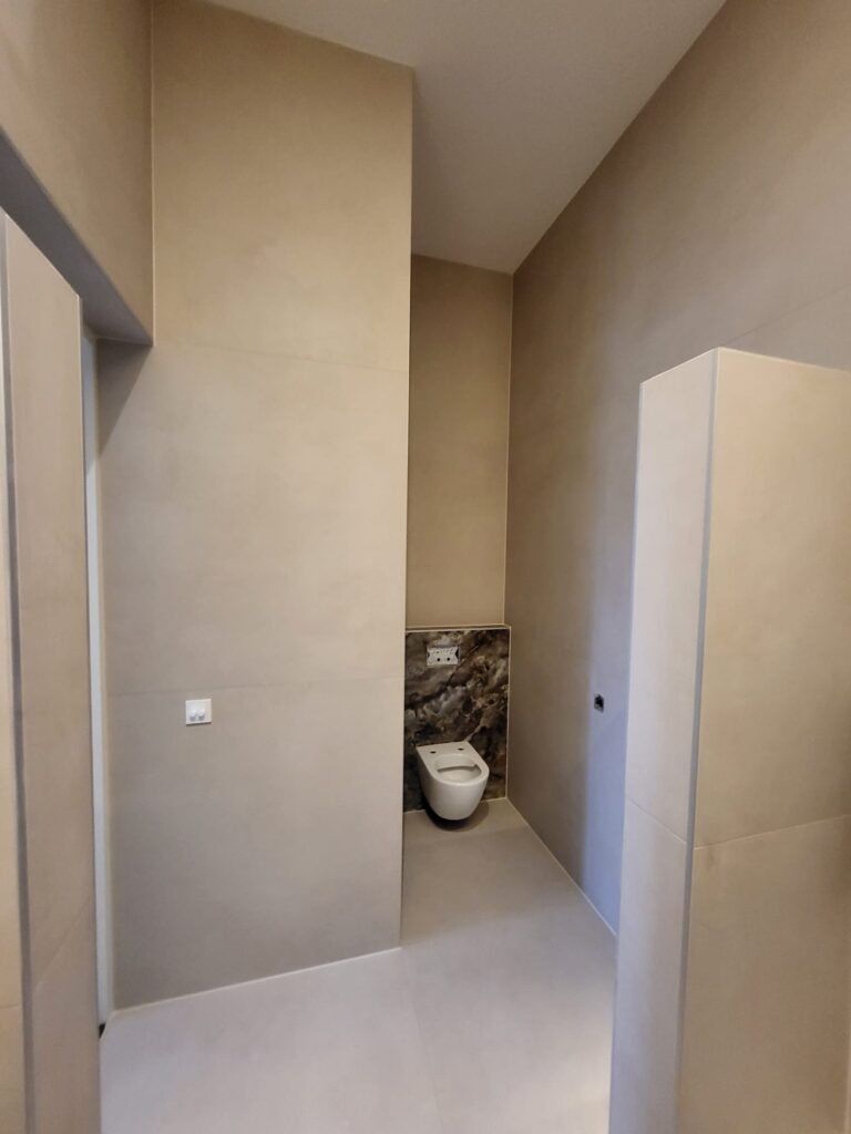 Minimalist toilet area with warm microcement-look walls and a marble-effect accent behind the toilet