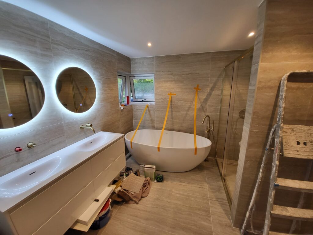 Bathroom renovation nearing completion with wood-look tiles, double round mirrors, freestanding bath and walk-in shower